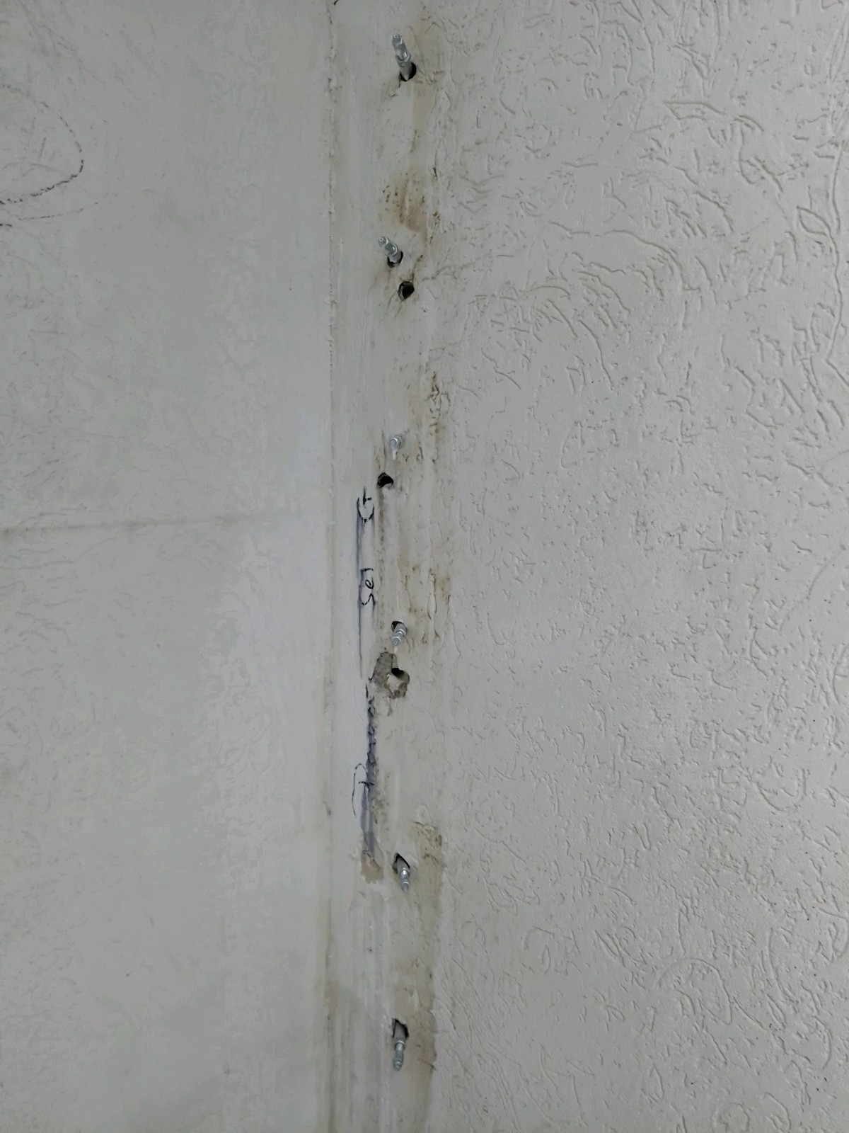 Senkrecht stehende Betonwand eines Brückenbauwerks mit Brettschalungsstruktur; mehrere parallel verlaufende schwarze Injektionsschläuche markieren den Rissbereich, dazwischen zahlreiche kleine Bohrlöcher für die Rissverpressung.